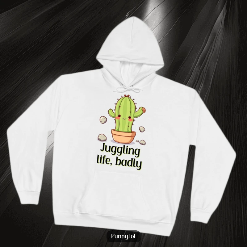 Funny hoodie featuring a clumsy cactus character juggling small stones, offering warmth and a humorous symbol of life's balancing acts.